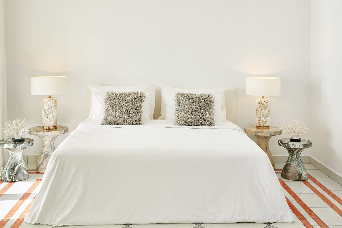 A neatly made bed with white linens, two decorative pillows, and two bedside tables with lamps and small vases.