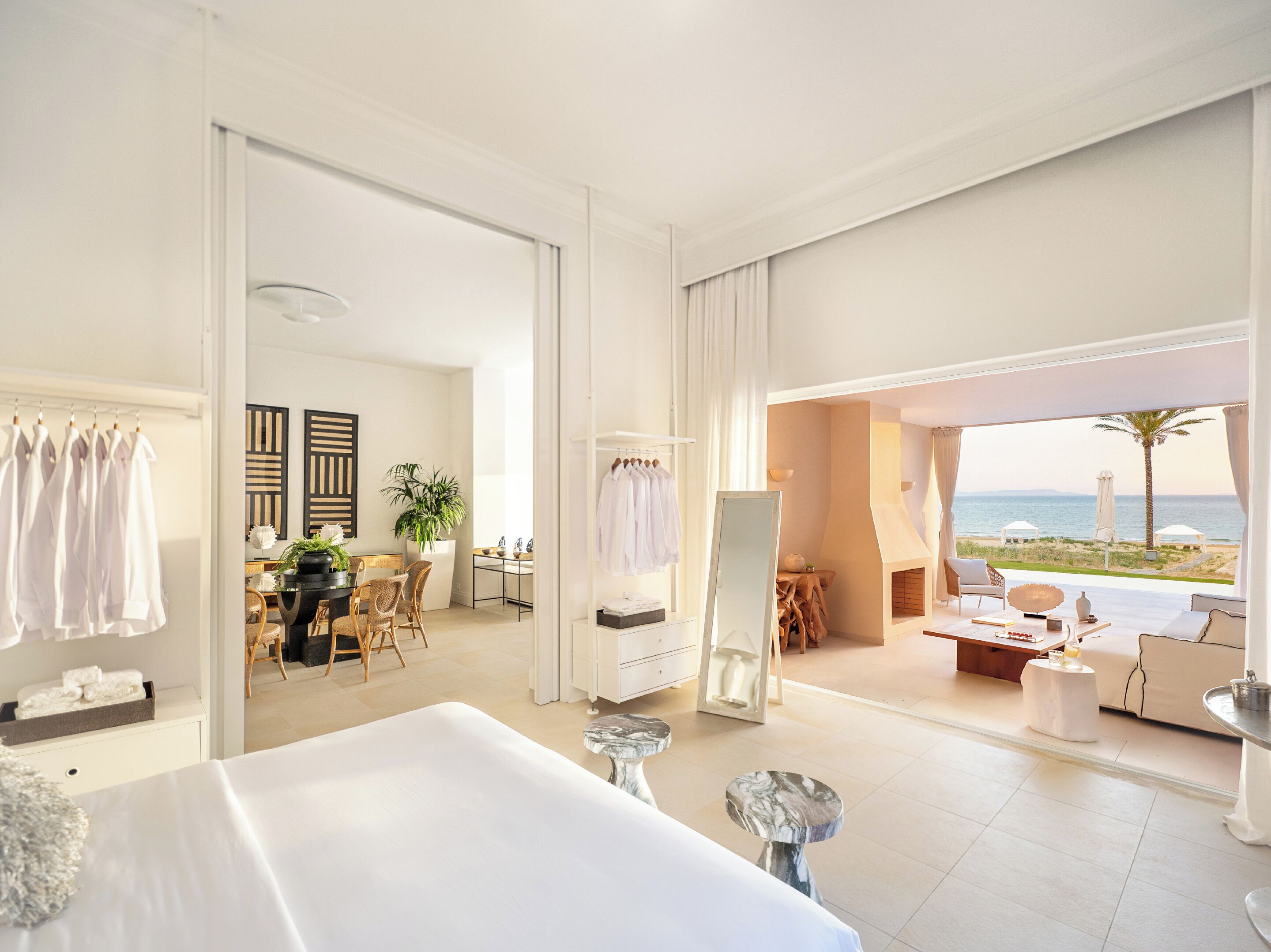 Een hotelkamer met een groot bed, een bureau, een stoel, een spiegel en uitzicht op het strand.