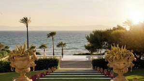 Un chemin menant à un balcon donnant sur la mer, bordé de jardinières décoratives et d’une balustrade blanche.