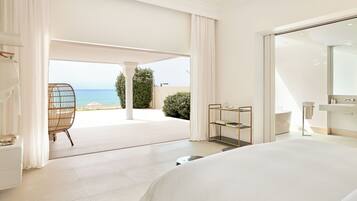 A hotel room with a bed, a chair, a small table, and a view of the beach.