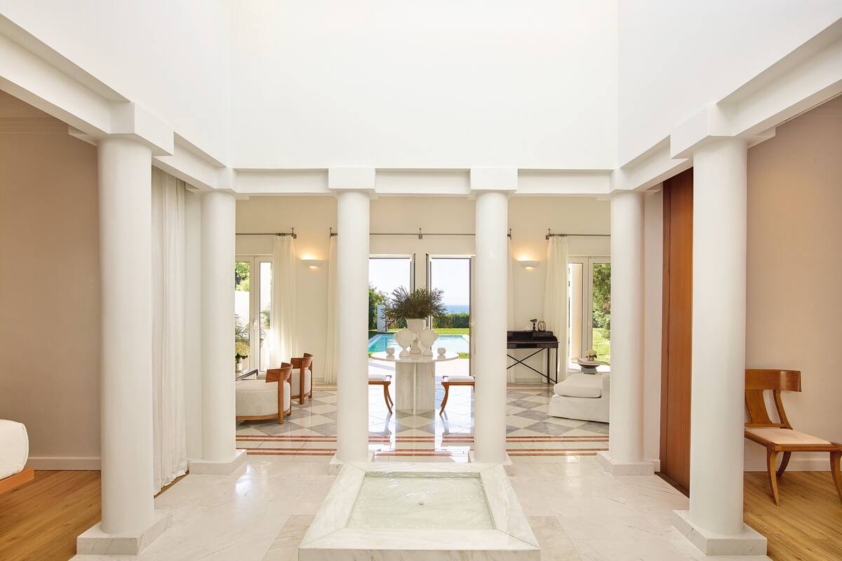A spacious indoor area with a pool view, white columns, and a marble floor.