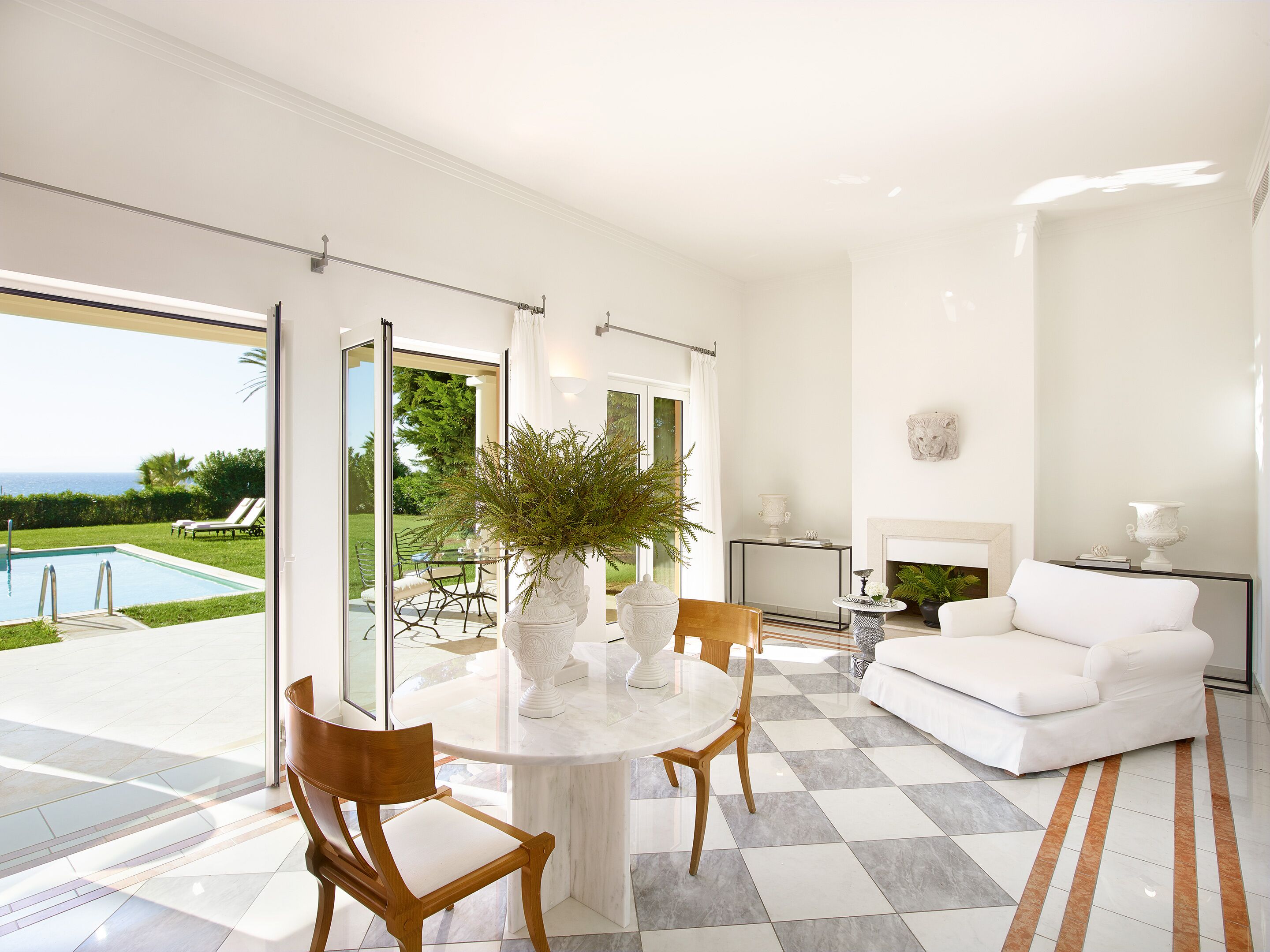 Amplia sala de estar con un sofá blanco, una mesa de centro redonda y vistas a una piscina y zonas verdes al exterior.