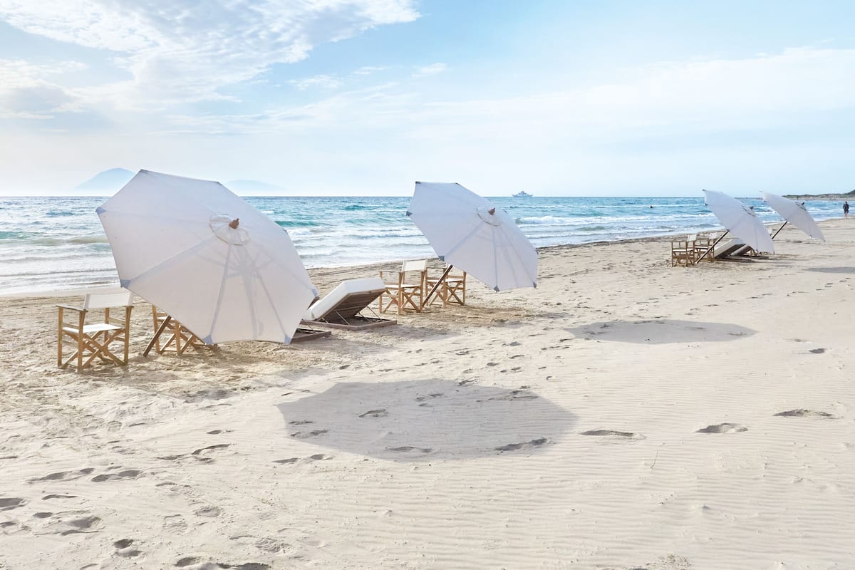 A beach with white umbrellas and wooden chairs arranged along the shoreline.