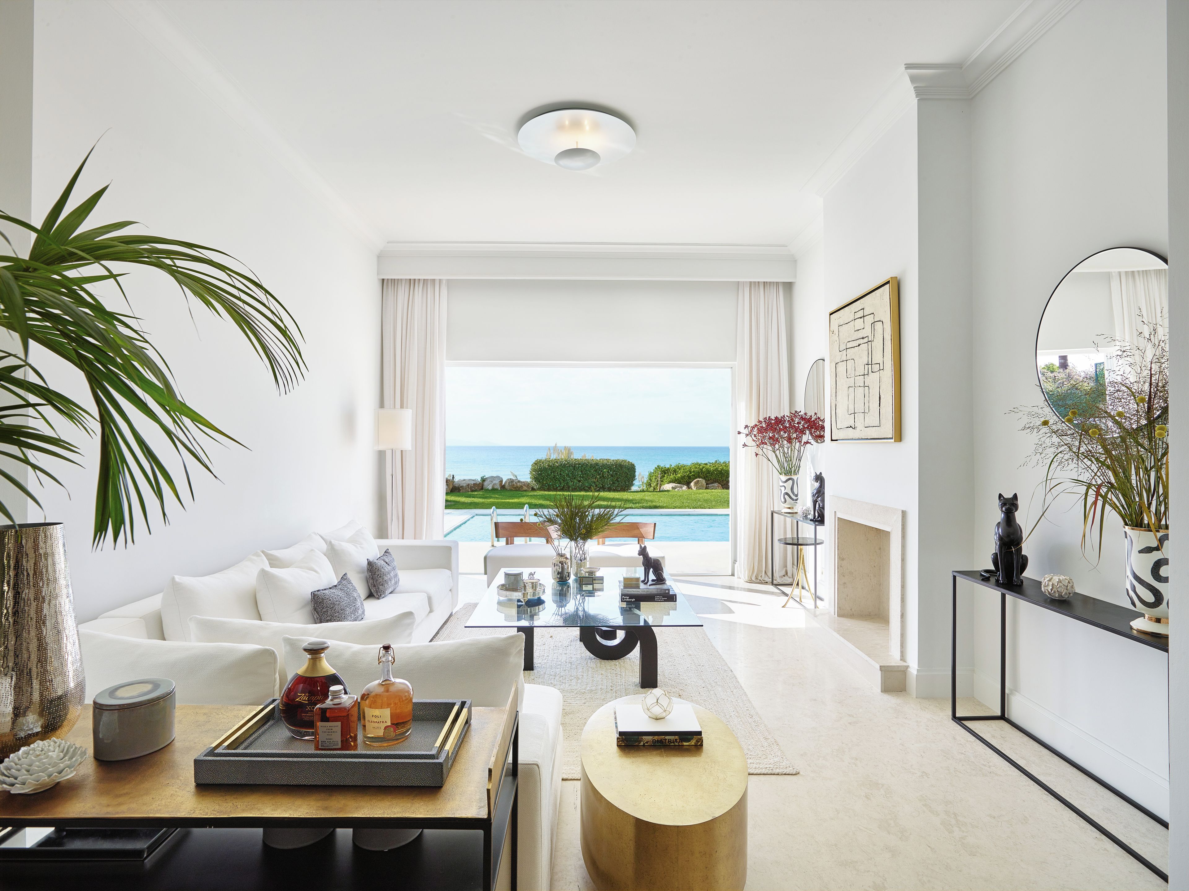 A modern living room with a white sofa, a glass coffee table, and a view of the sea.