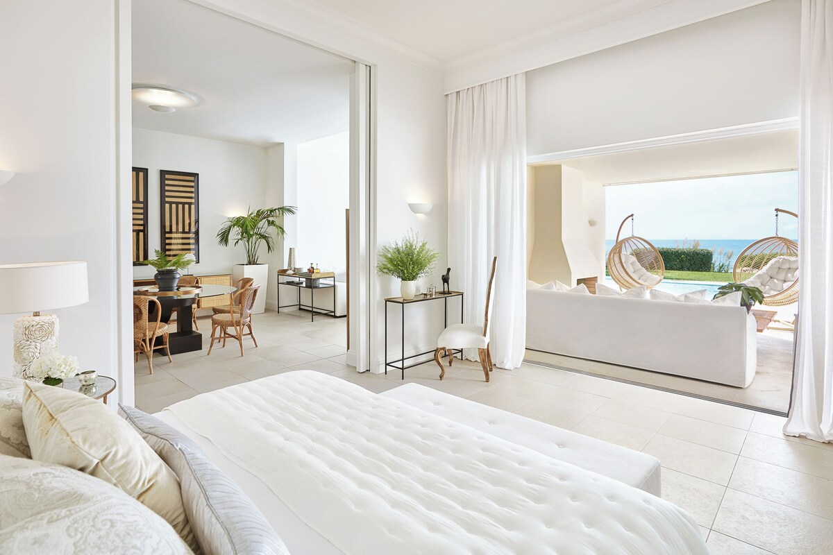 A spacious bedroom with a large bed, a sitting area with a view, and a dining area with a view.