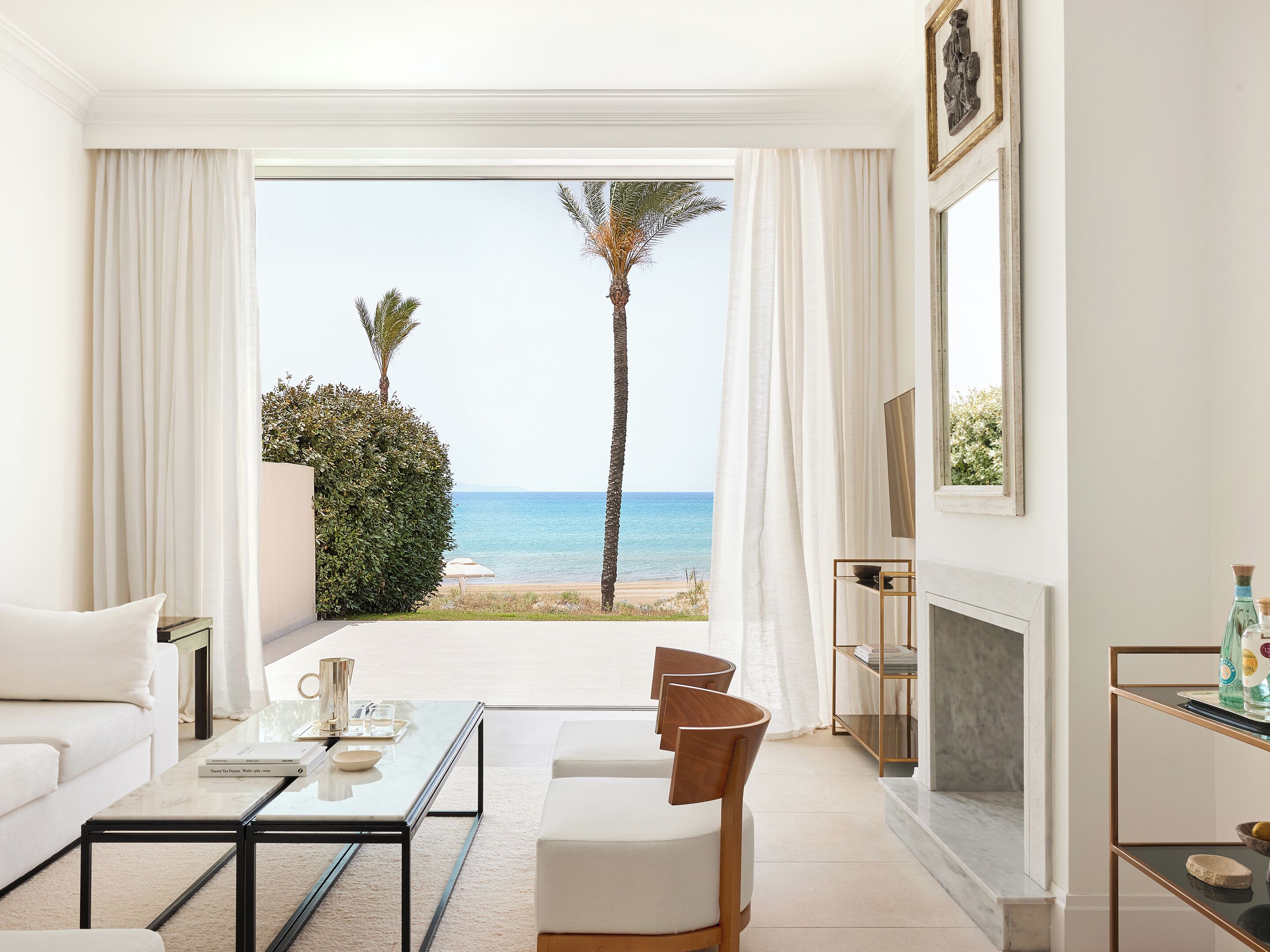 A modern living room with a view of the beach, a fireplace, and a coffee table with books.