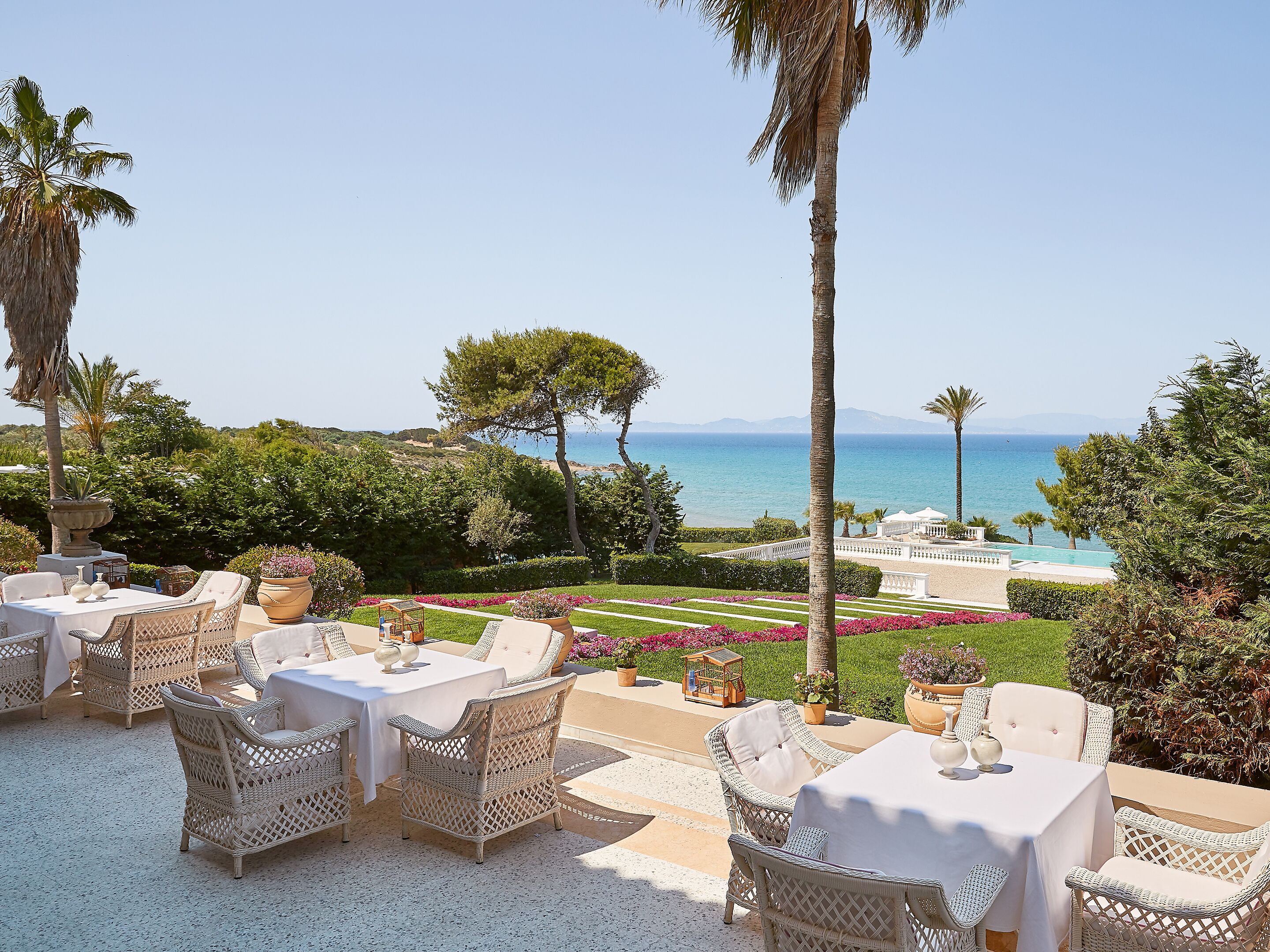 An outdoor dining area with wicker furniture and a view of the sea.