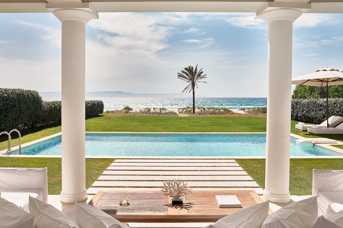 A poolside area with a view of the ocean, white columns, and lounge chairs.