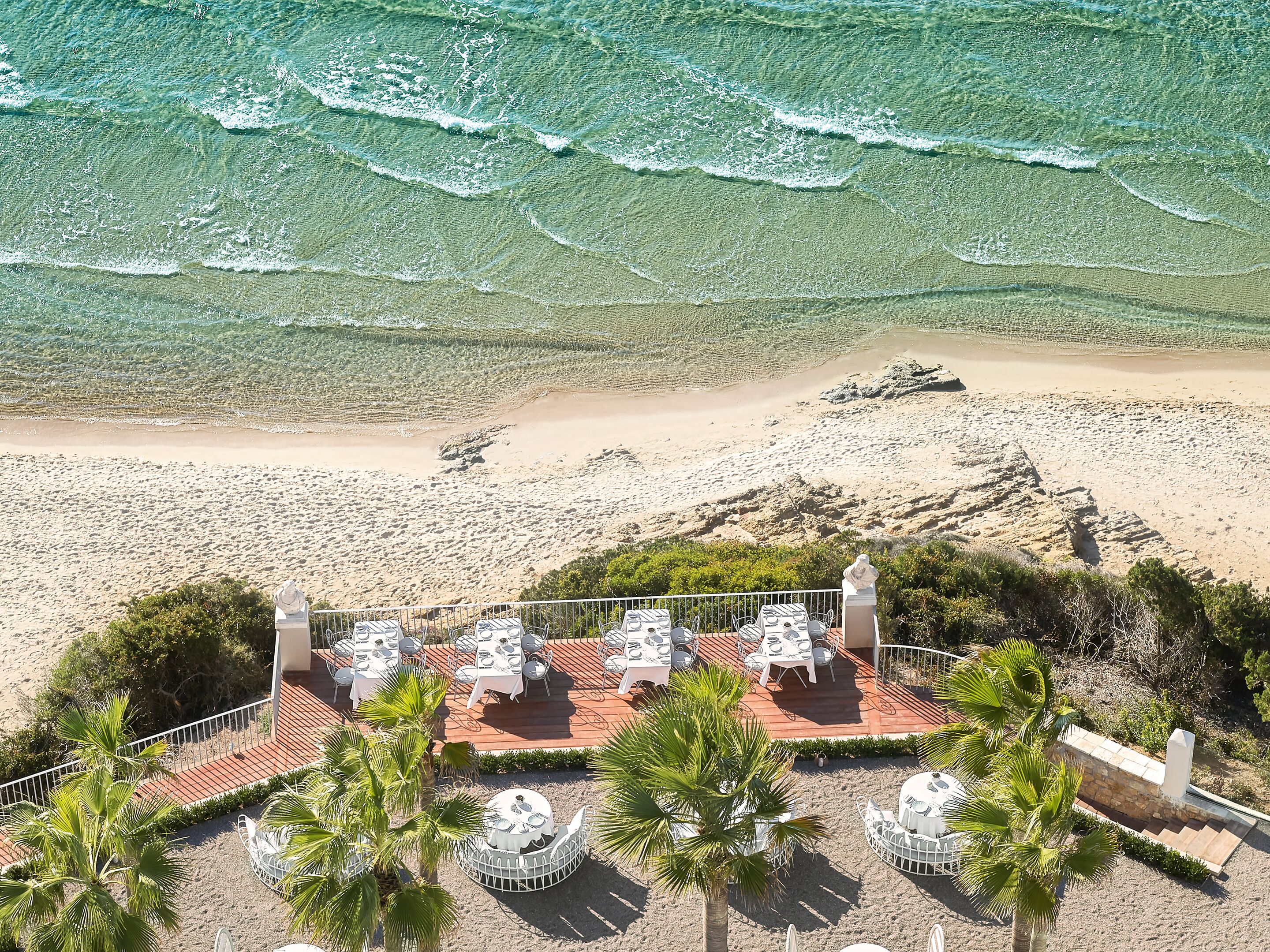 Un espace extérieur aménagé pour les repas, avec des tables et des chaises, offrant une vue sur une plage et l’océan.