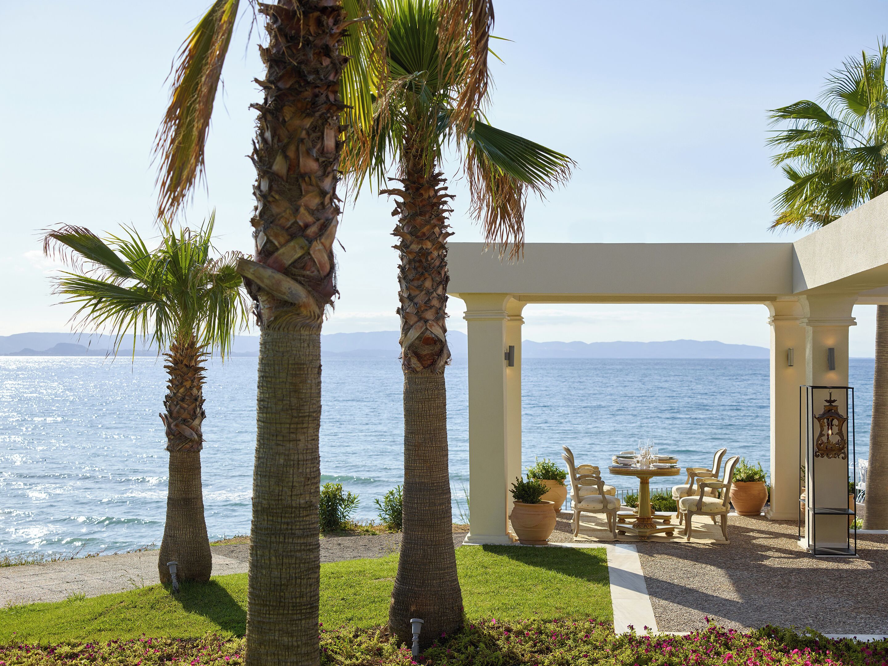 Un espace extérieur aménagé avec des sièges, situé en bord de mer, agrémenté de palmiers, d’une pergola et offrant une vue sur l’océan.