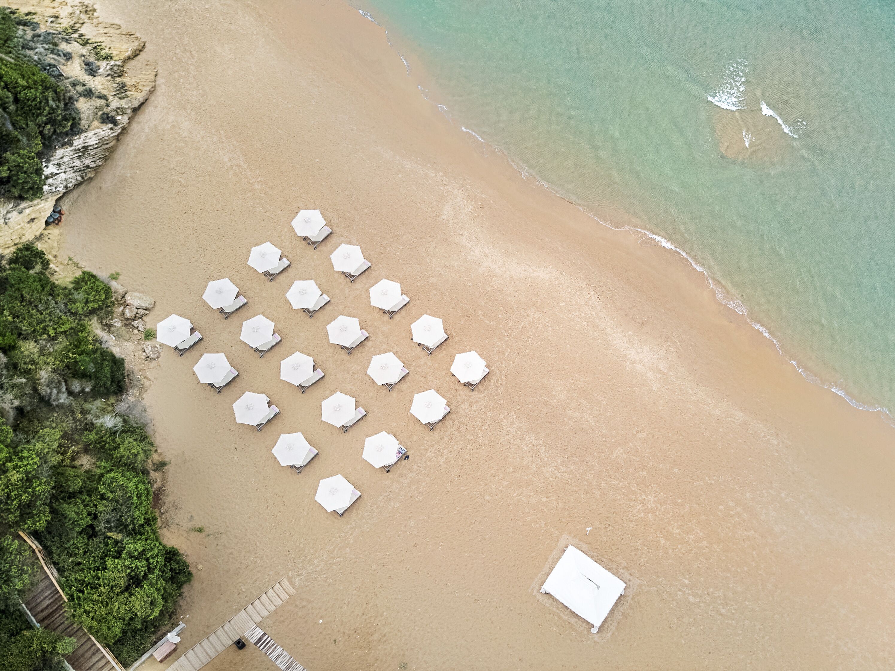 An aerial view of a beach with rows of white umbrellas and a small white building.