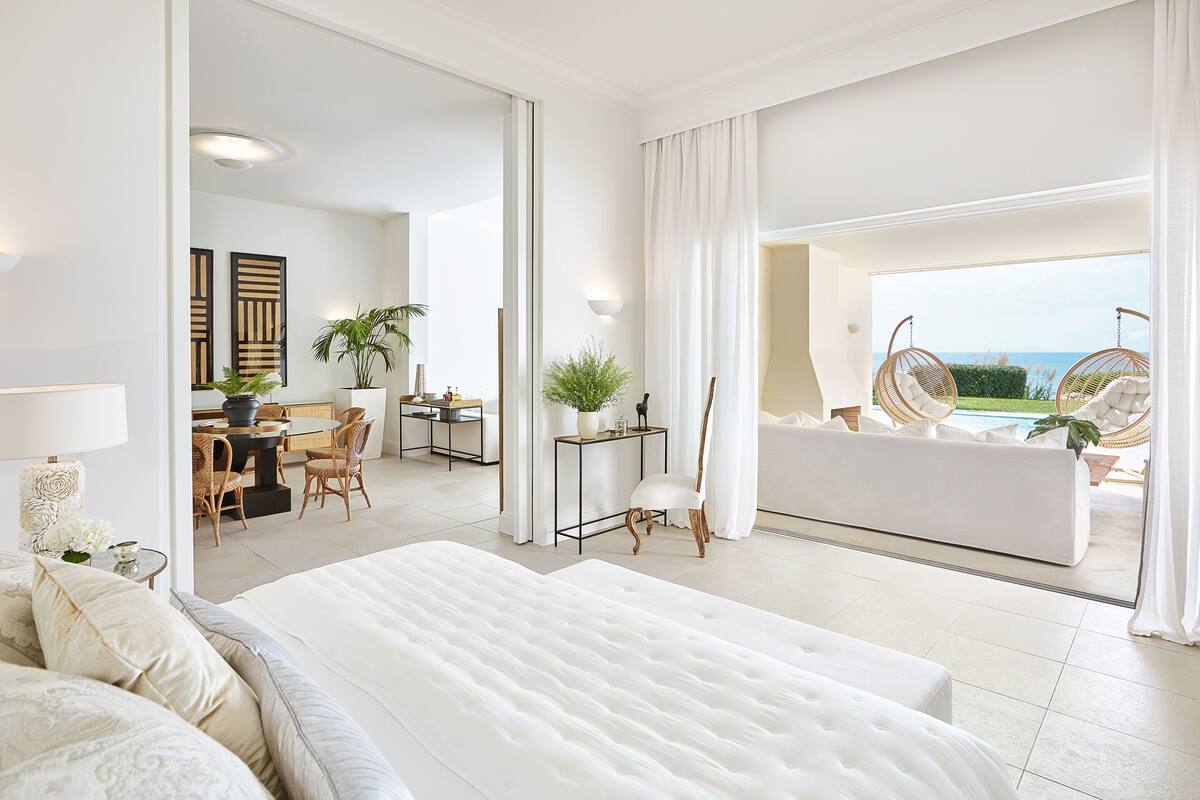 A spacious bedroom with a large bed, a sitting area with a sofa and chairs, and a view of the outdoors.
