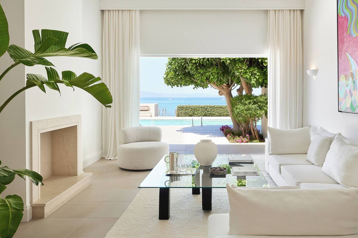 A modern living room with a white sofa, a glass coffee table, and a view of the sea.