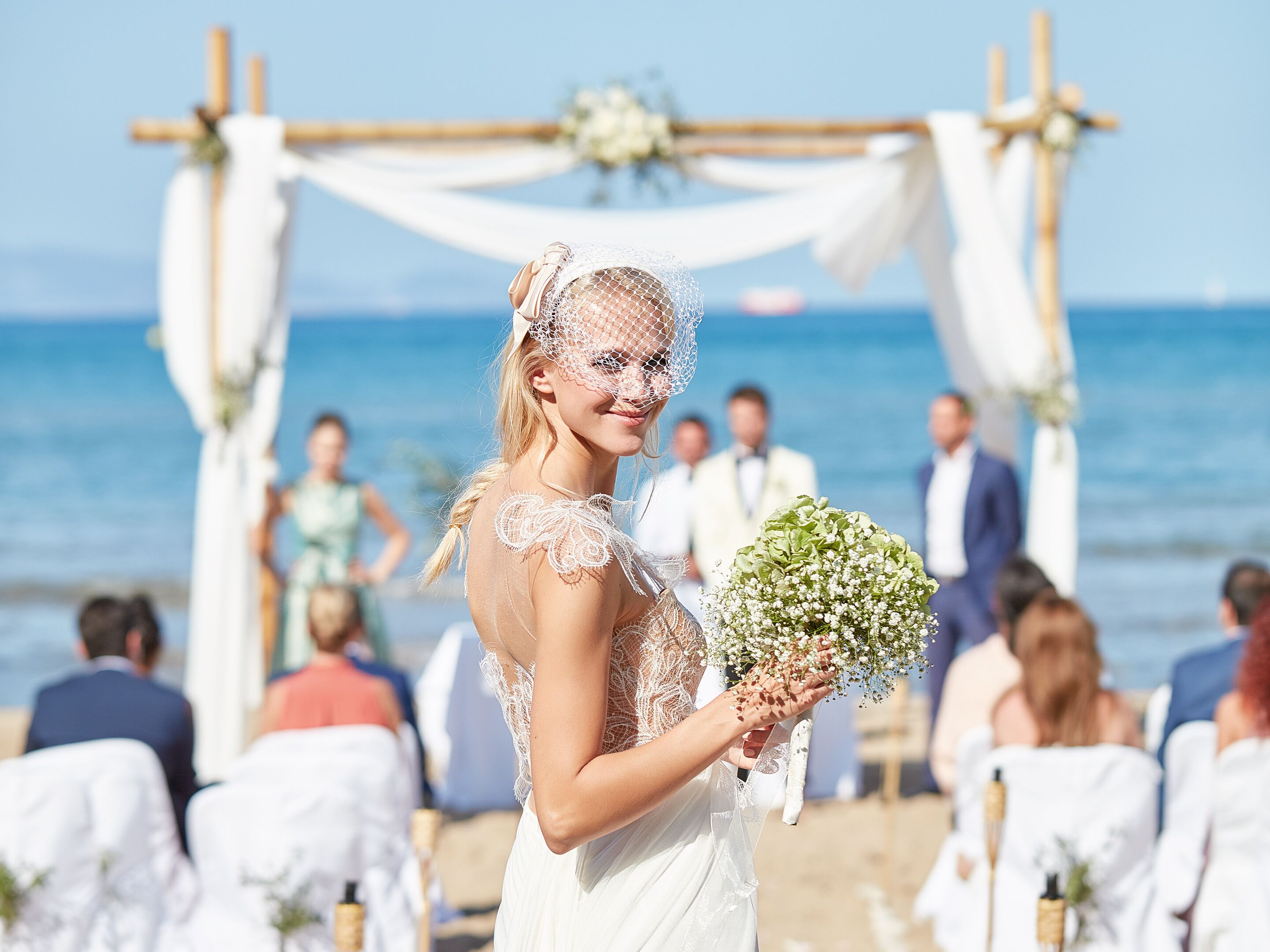 Une cérémonie de mariage sur une plage, avec une arche en bois et des invités assis sur des chaises blanches.