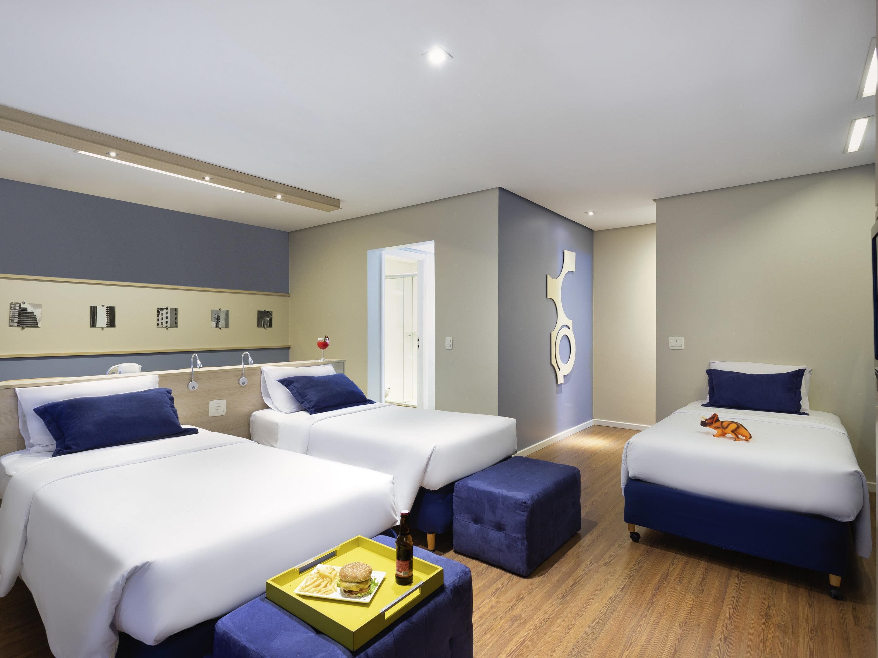 A hotel room with three beds, a wooden floor, and a wall-mounted artwork.