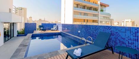 A rooftop pool with lounge chairs and a view of surrounding buildings.