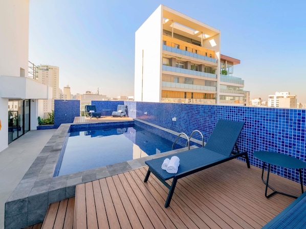 A rooftop pool with lounge chairs and a view of surrounding buildings.