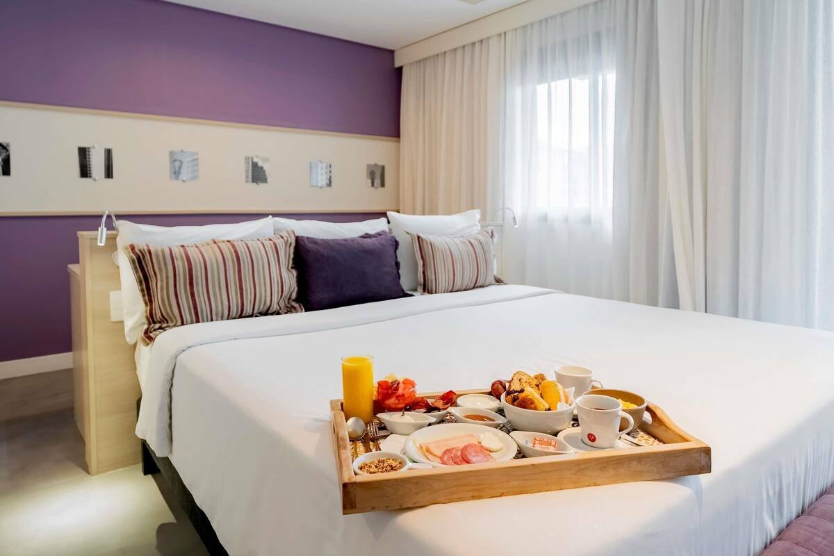 Una habitación de hotel con una cama grande, una mesita de noche de madera y una bandeja de desayuno sobre la cama.