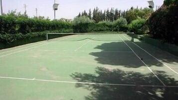 Un campo da tennis all'aperto circondato da vegetazione e pali elettrici.