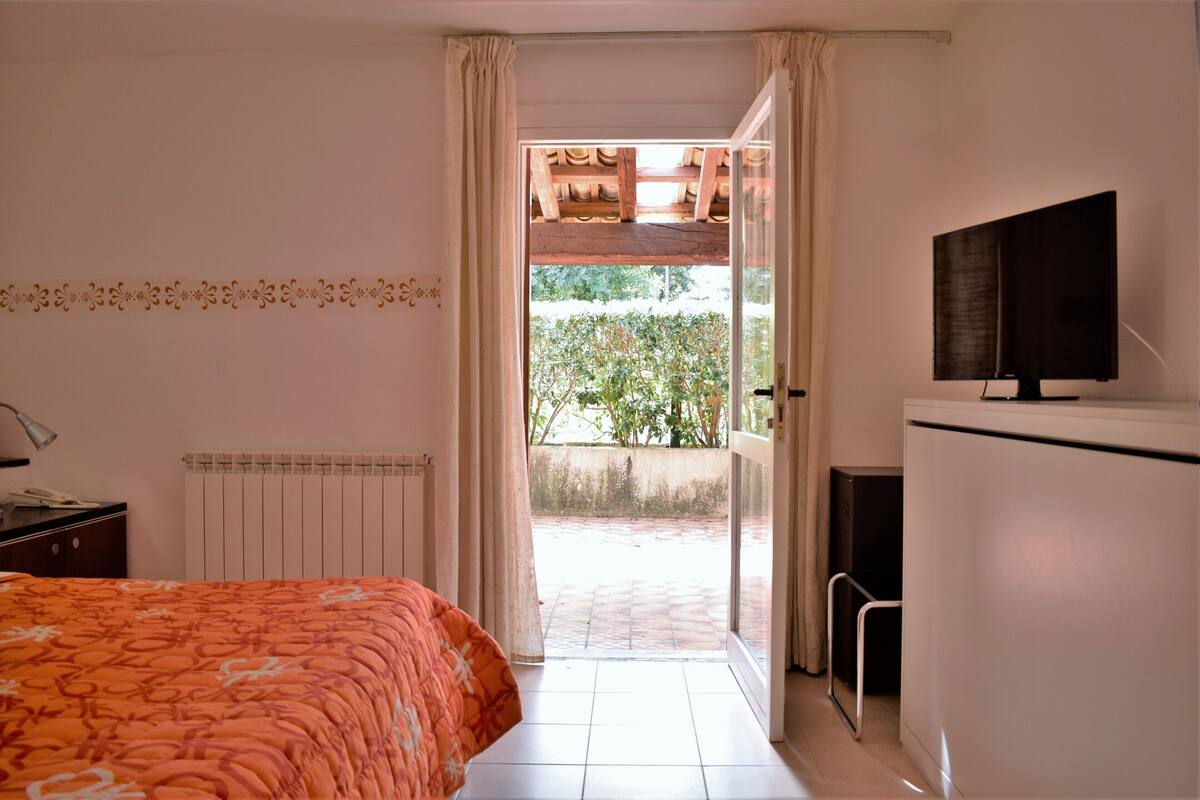 A bedroom with a bed, a television, a radiator, and a view of the outdoors.
