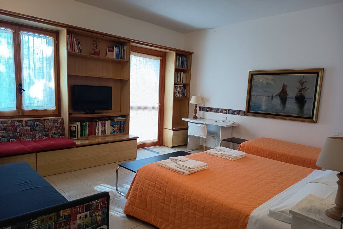 A hotel room with a bed, a desk, a television, a bookshelf, and a window with curtains.