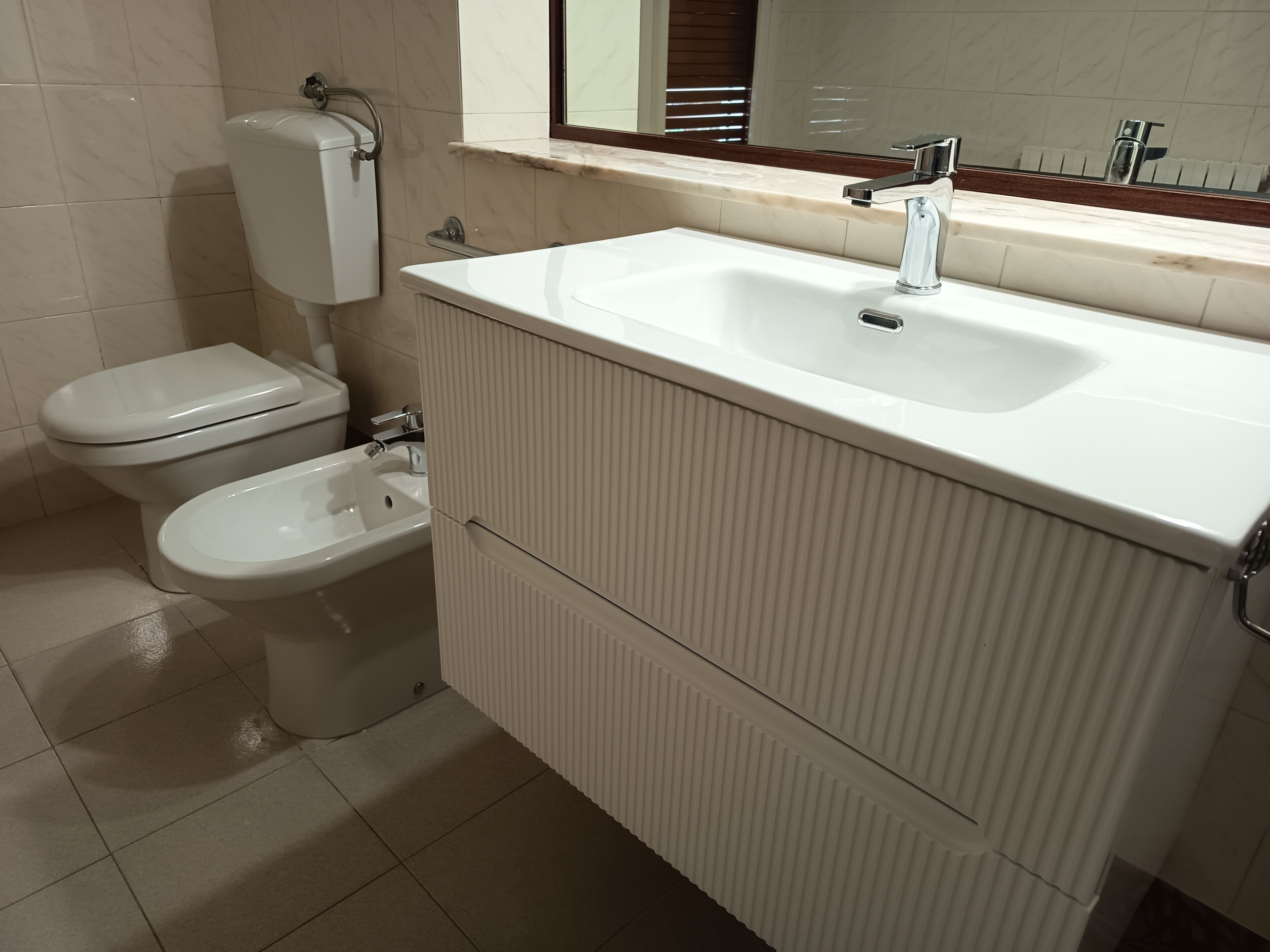 A bathroom with a toilet, bidet, and a sink with a mirror above it.