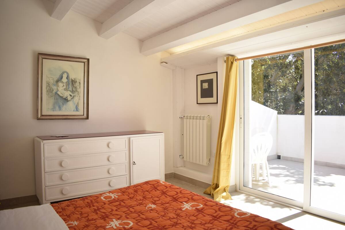 A bedroom with a bed, a dresser, a radiator, and a sliding glass door to a balcony.
