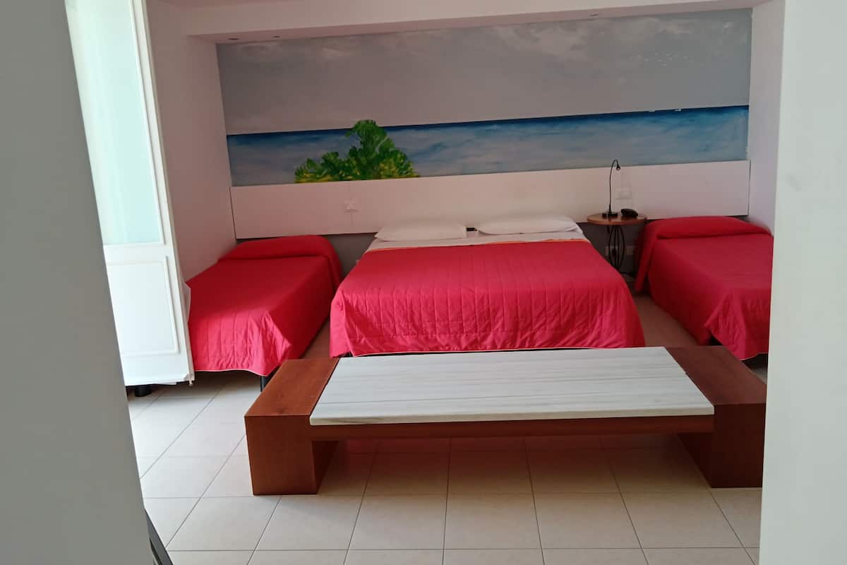 A bedroom with a large bed, two smaller beds, a painting of a beach, and a nightstand.
