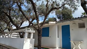 Un bâtiment blanc avec des portes bleues, un mur de pierre et un arbre.