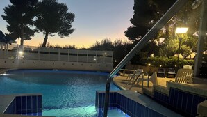 Une piscine avec une terrasse carrelée, une échelle en métal et des chaises.