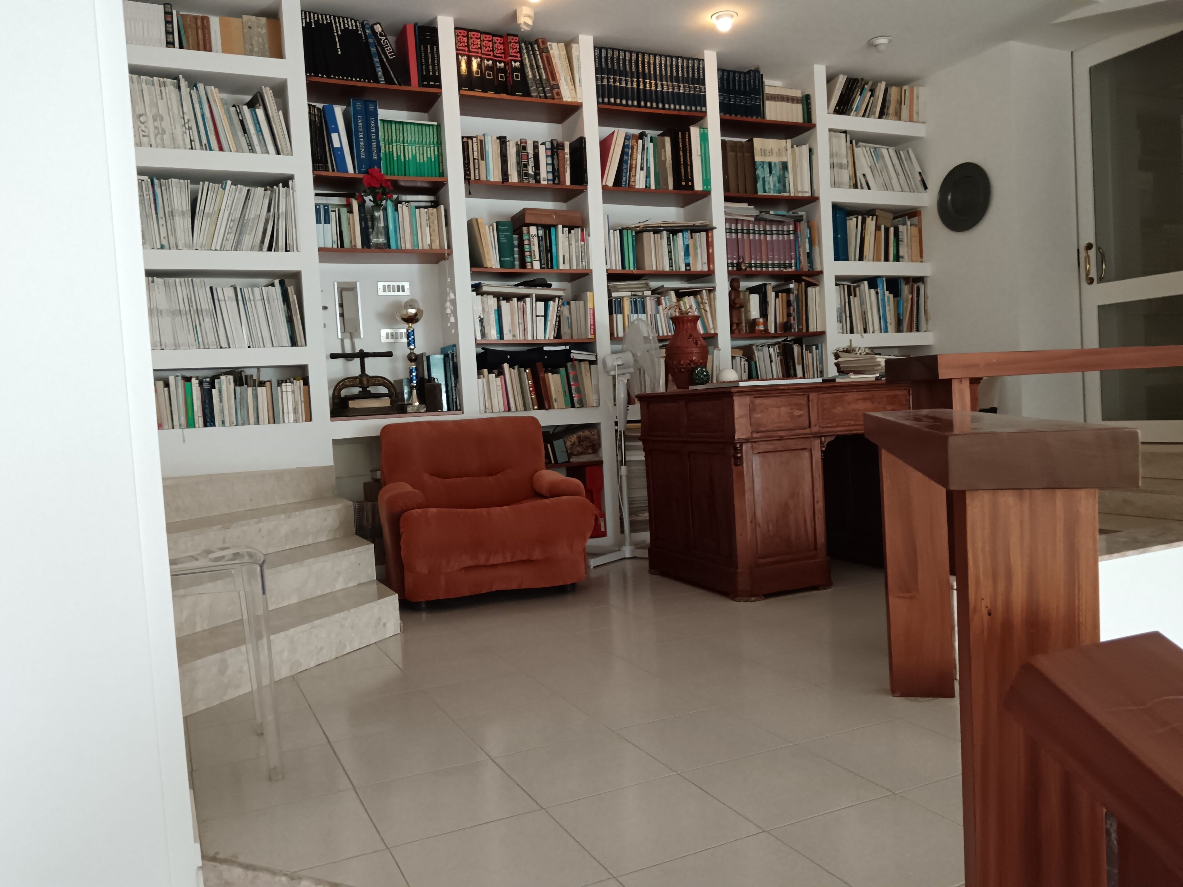A library with bookshelves, a wooden desk, and a red armchair.