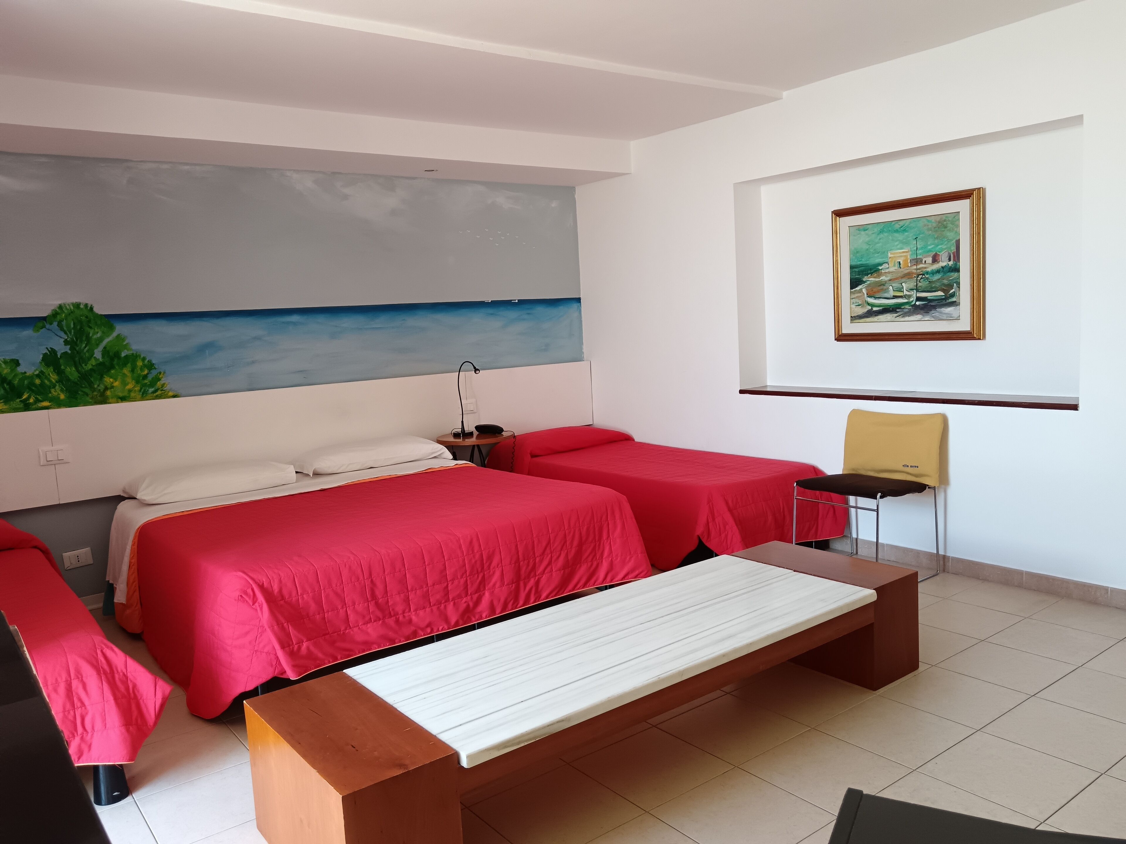 Habitación de hotel con dos camas, un escritorio, una silla, un cuadro y vista al mar.