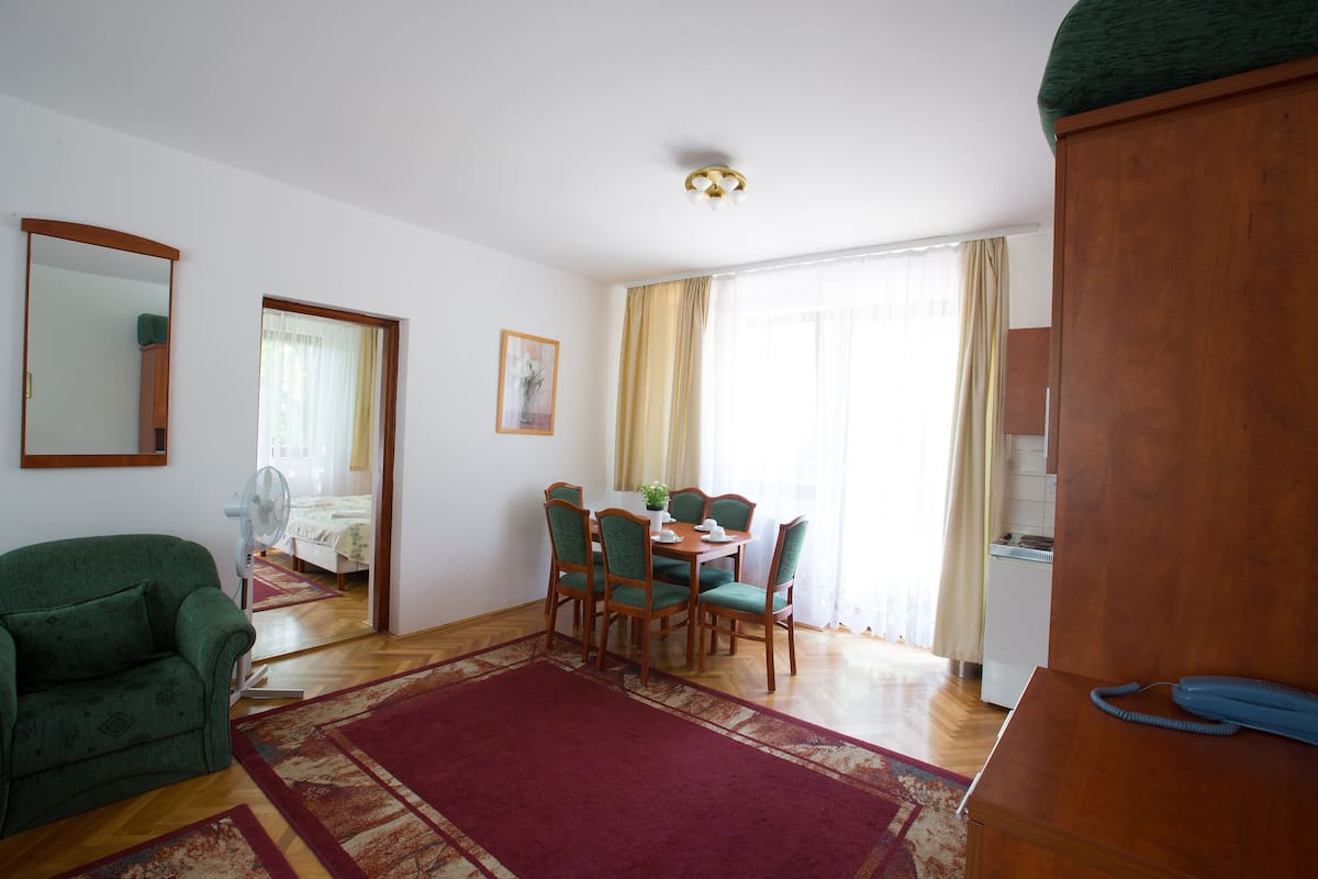 A living room with a dining area, a green sofa, a wooden cabinet, and a blue telephone.