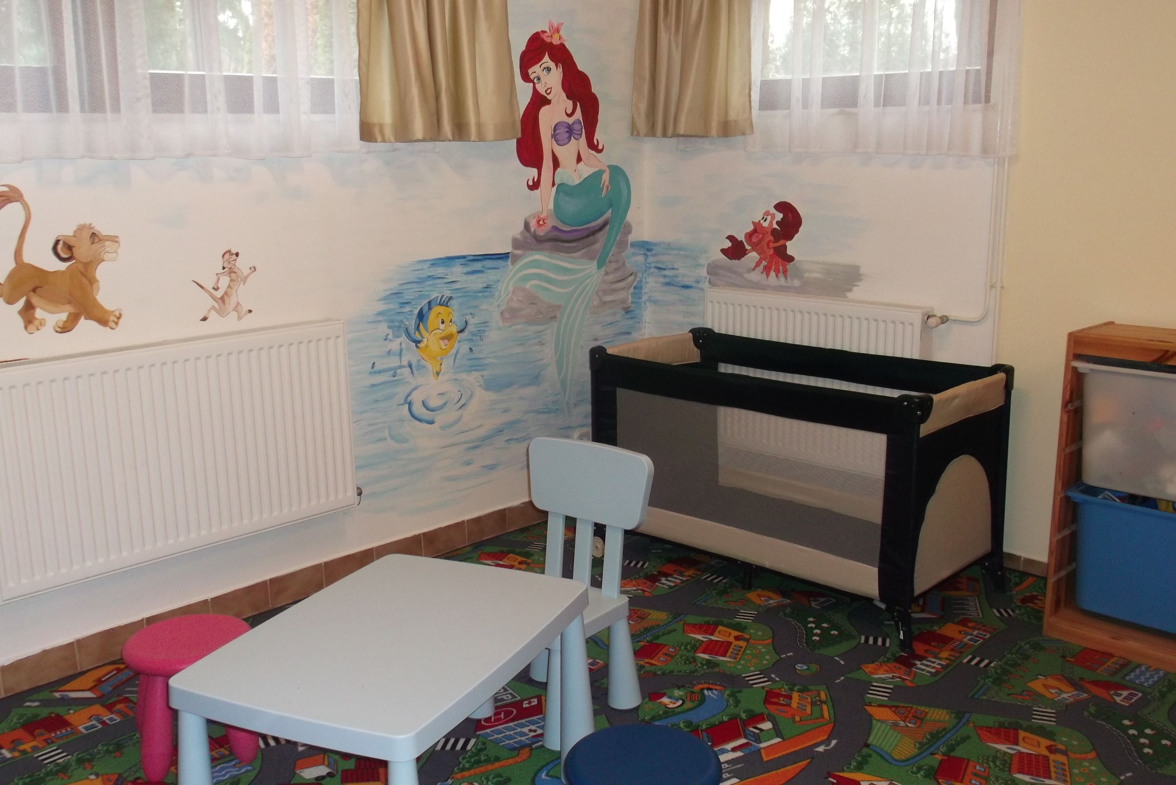 A child's playroom with a mermaid mural, a playpen, a table, and chairs.