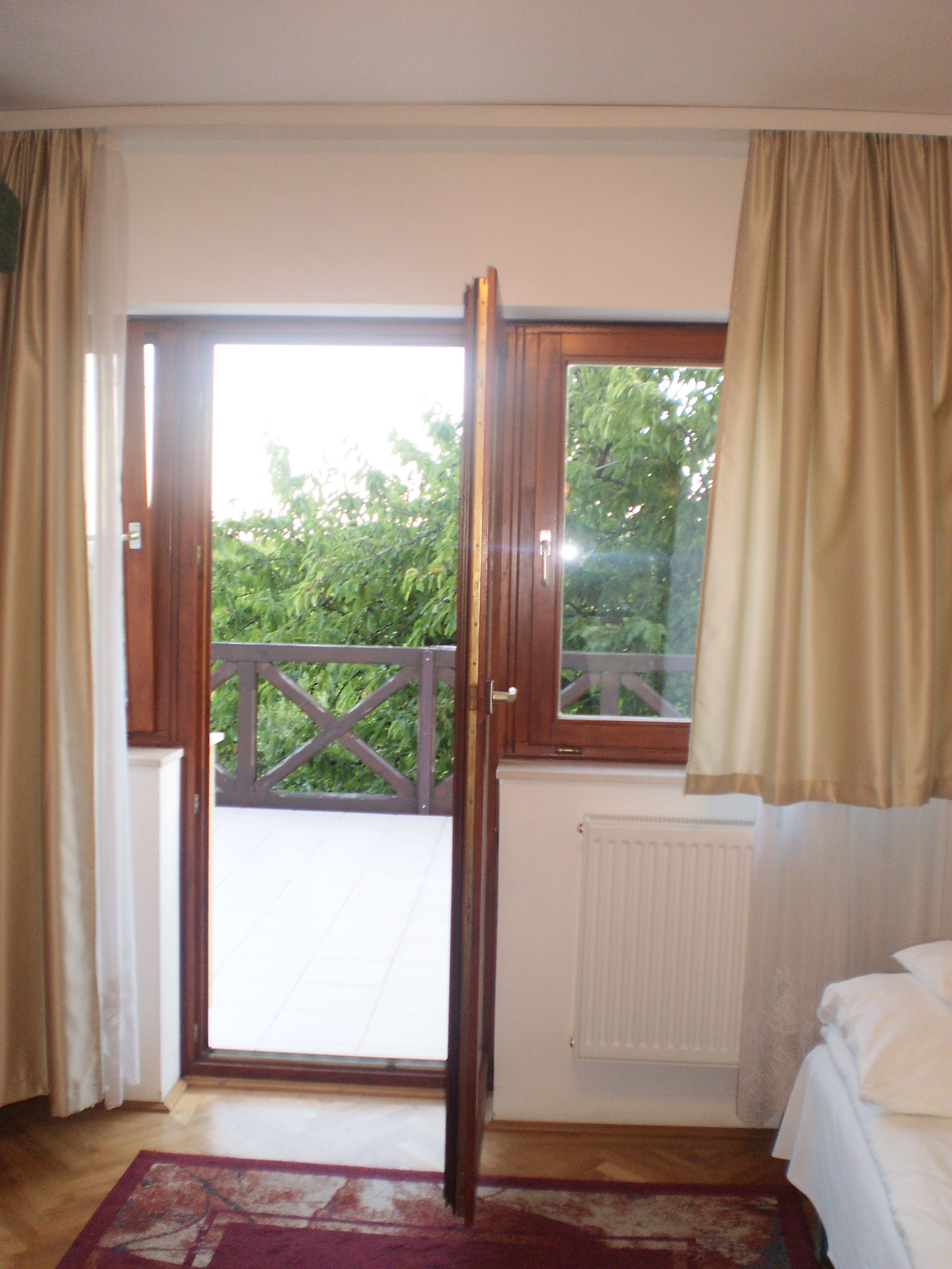 A room with a wooden door leading to a balcony, a bed with white bedding, and a radiator.
