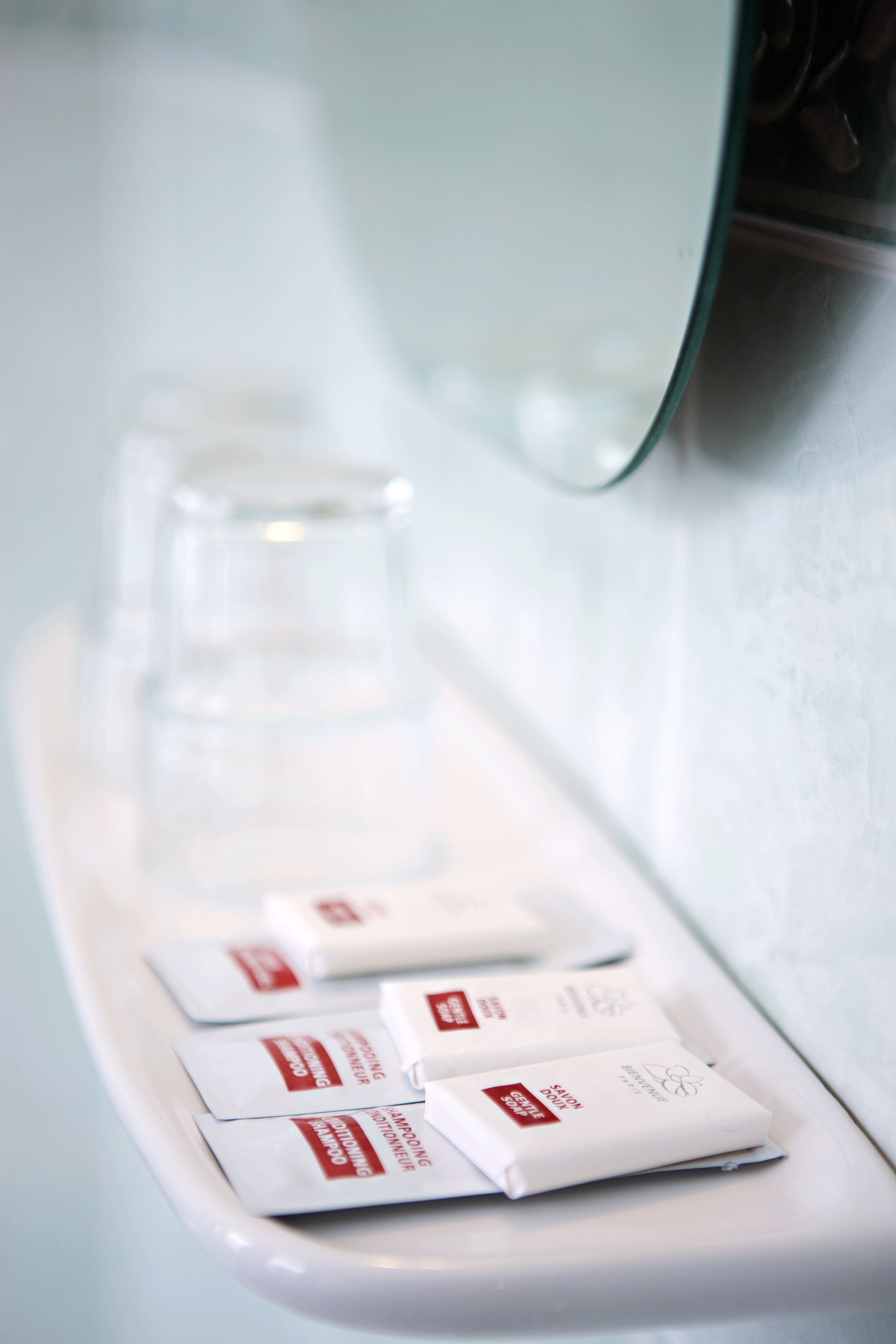 Une salle de bain avec un lavabo blanc, un miroir et des articles de toilette, notamment du shampoing et de l’après-shampoing.