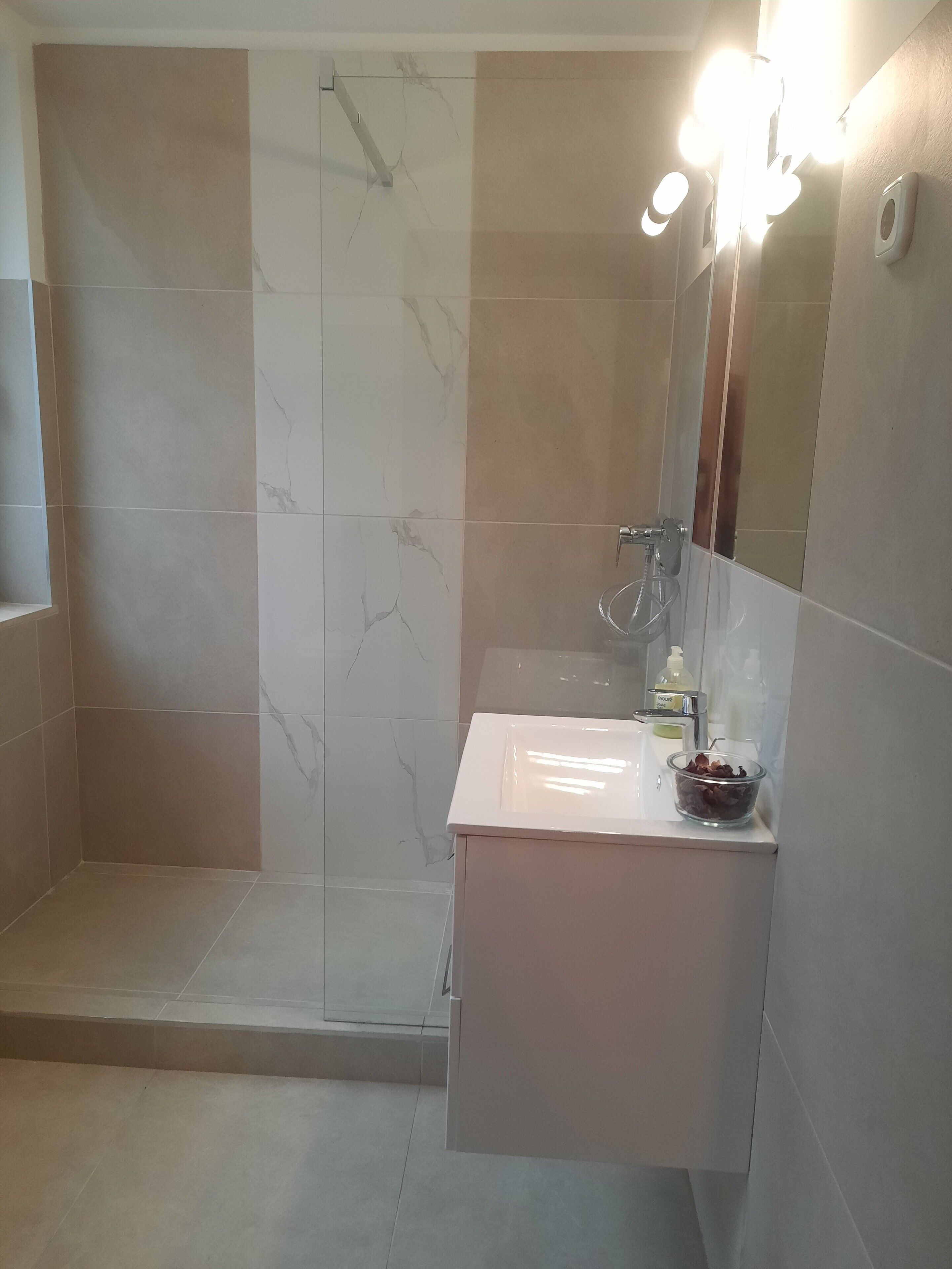 Un baño moderno con cabina de ducha de vidrio, un lavabo blanco y un espejo con iluminación.