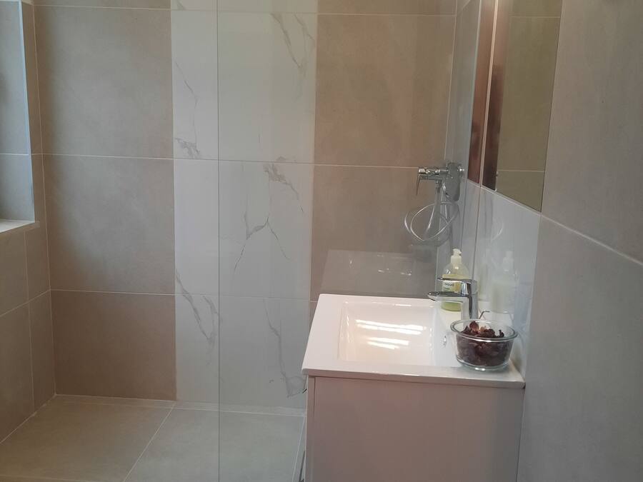 Un baño moderno con cabina de ducha de vidrio, un lavabo blanco y un espejo con iluminación.