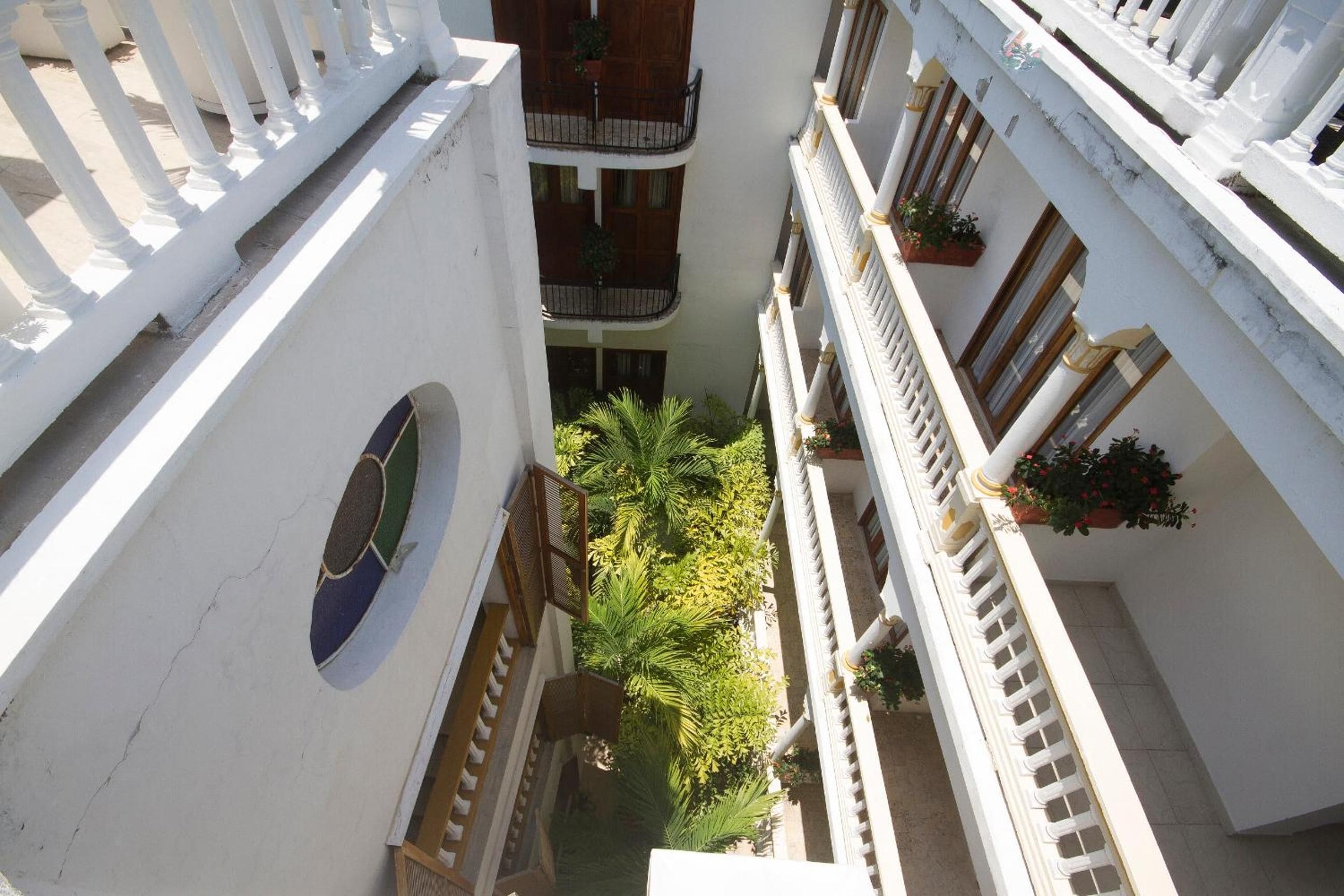 A multi-level building with balconies, a central courtyard with palm trees, and potted plants.