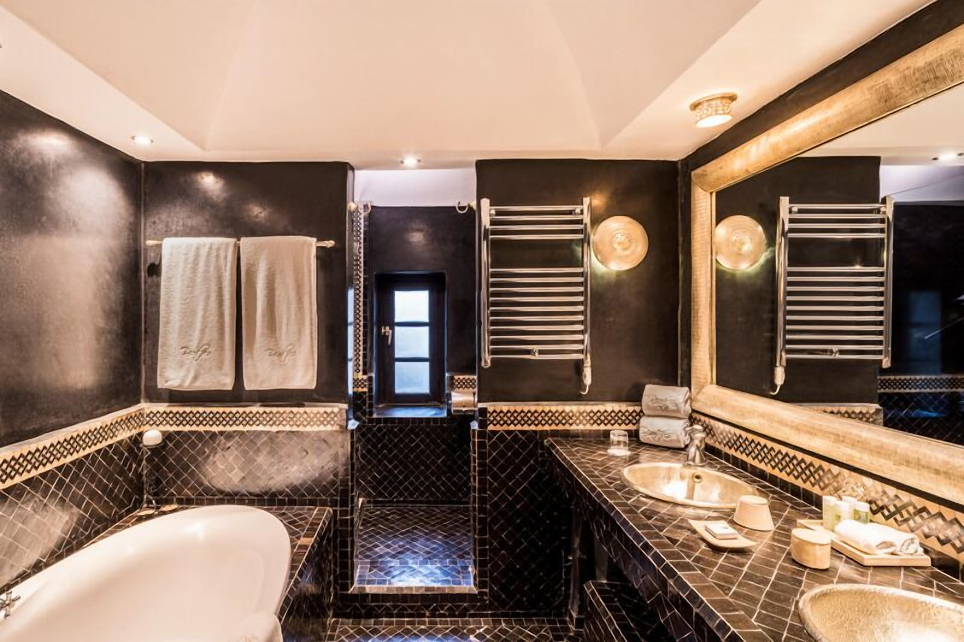 A modern bathroom with a black and white tiled floor, a large mirror, and a bathtub.