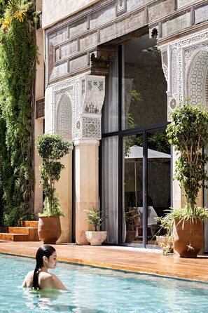 A pool area with a view of a building with intricate tile work and large potted plants.