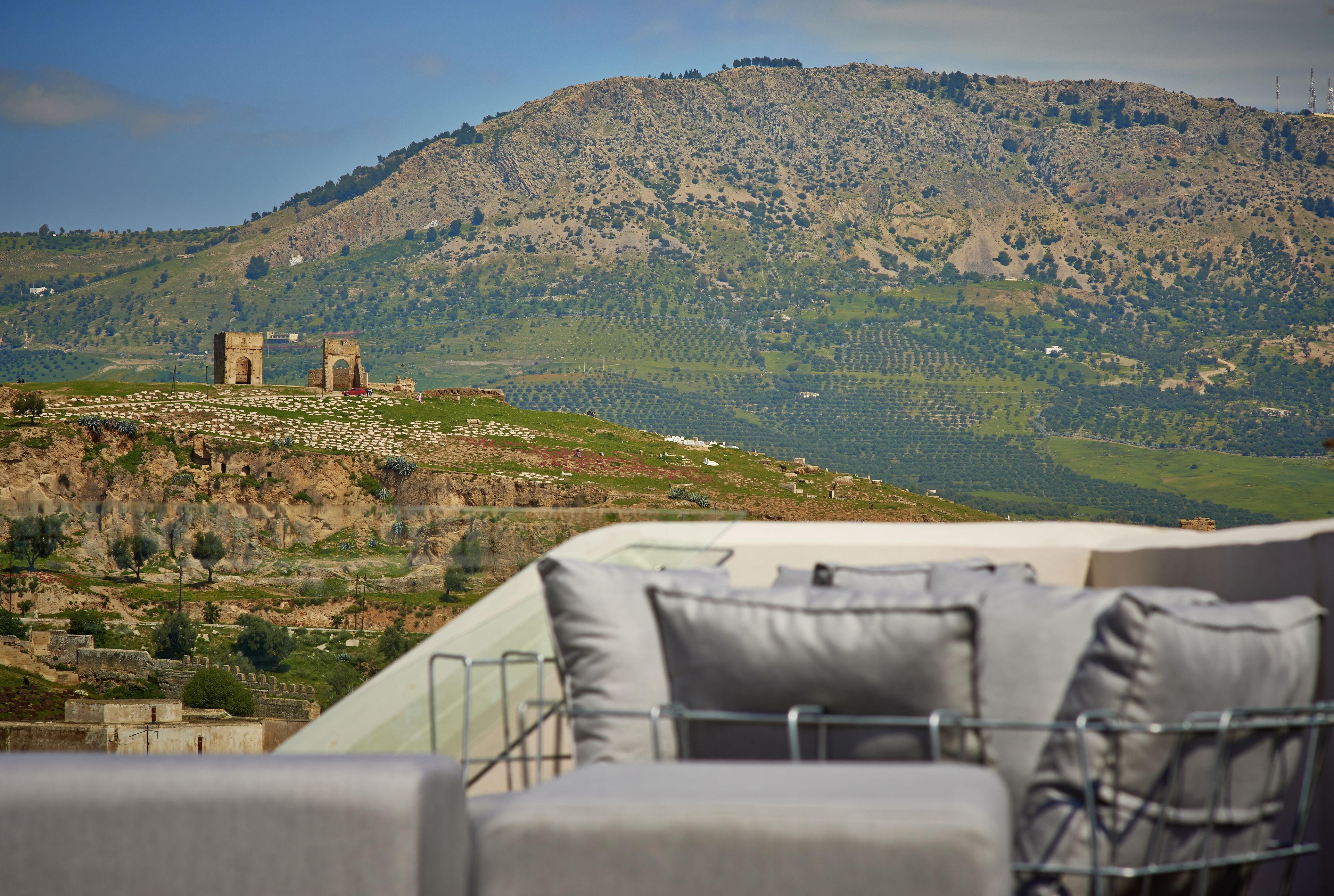 Terraço com vista para uma colina com ruínas e oliveiras.