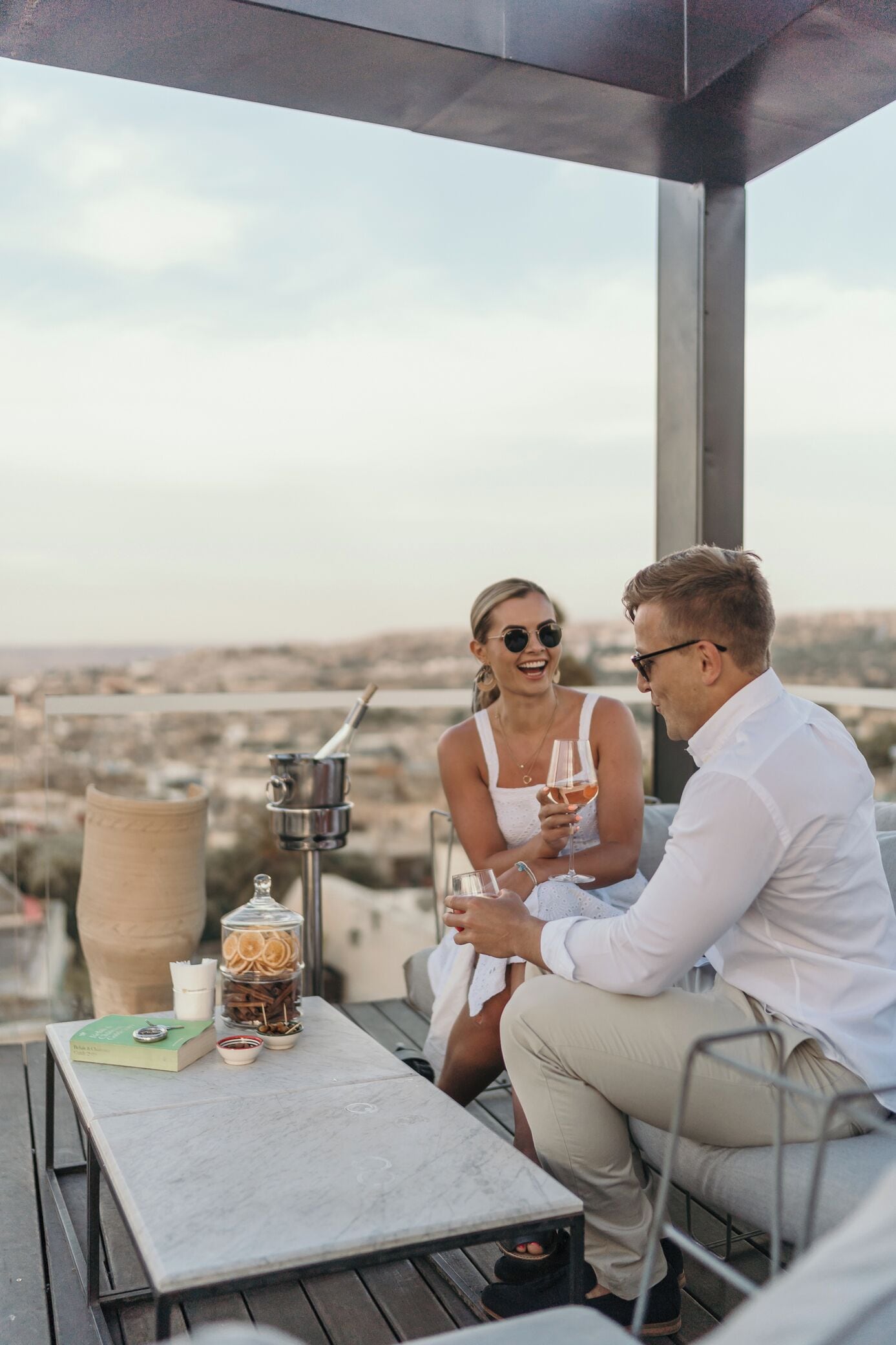 A couple sitting at an outdoor table with a city view, a book, and a candle holder.