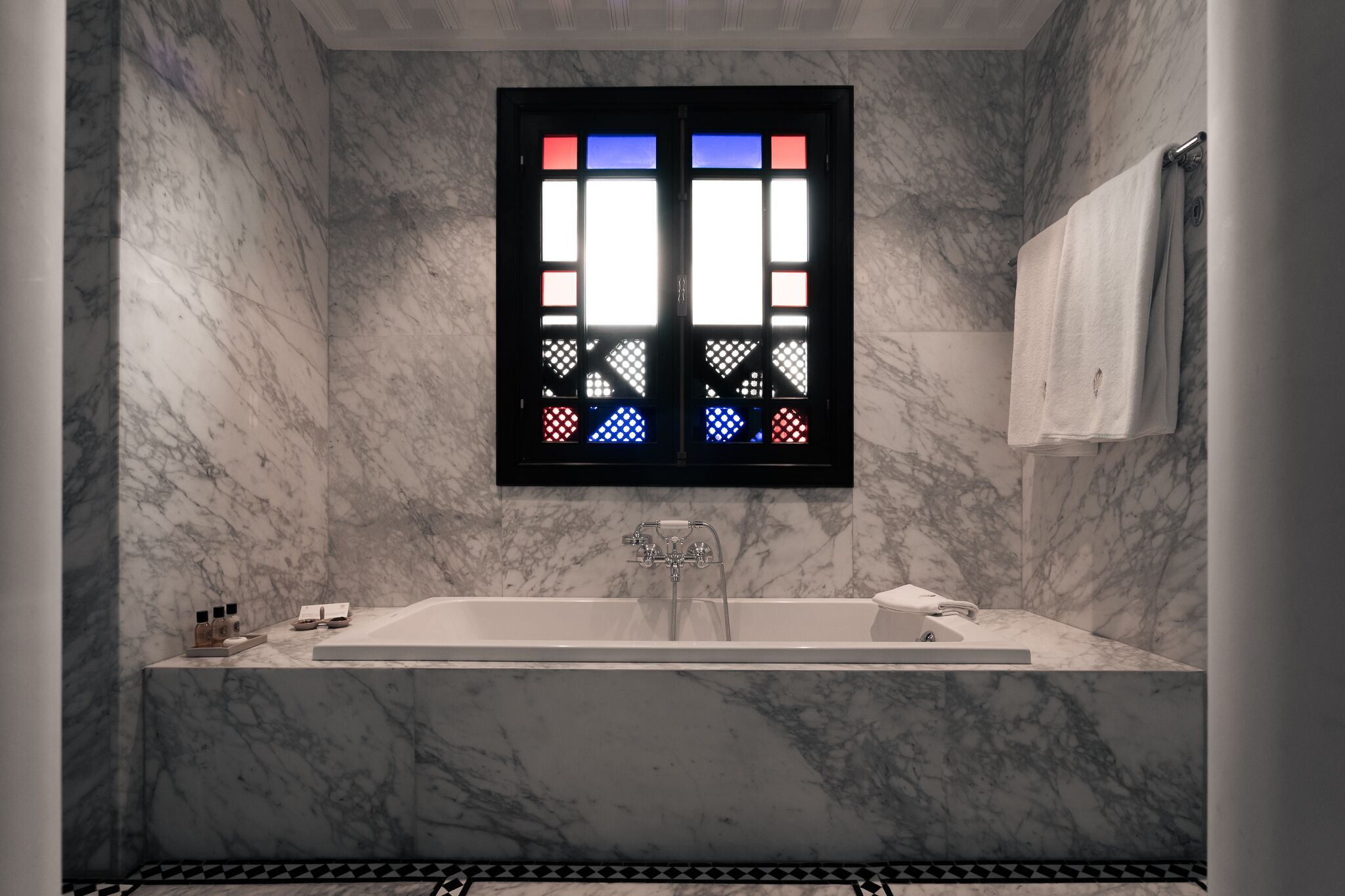 A modern bathroom with a large bathtub, a window with colorful stained glass, and marble walls.