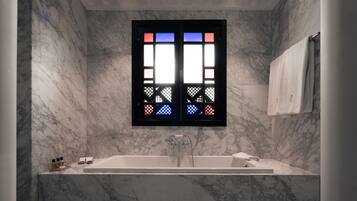 A modern bathroom with a large bathtub, a window with colorful stained glass, and marble walls.