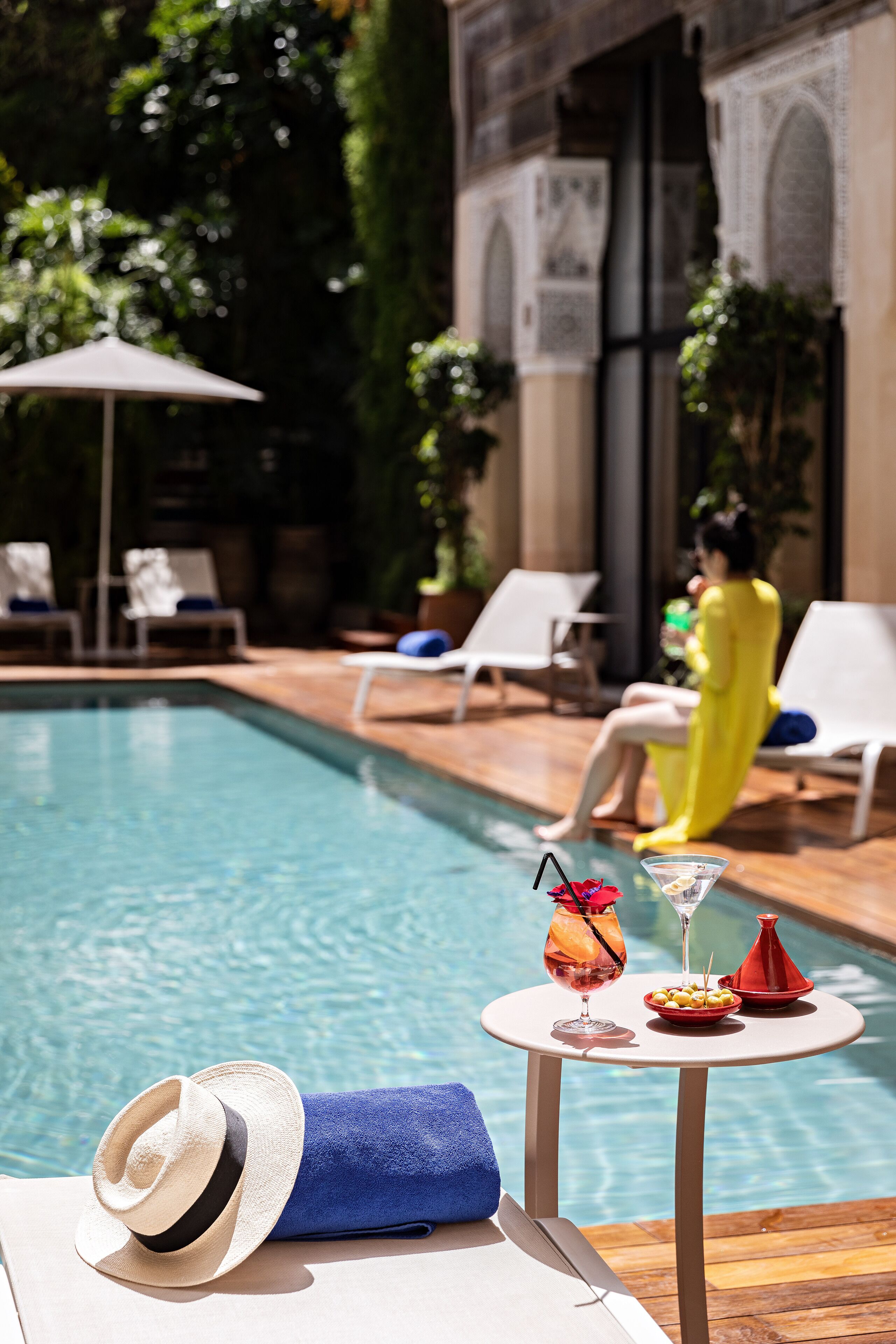 A poolside area with lounge chairs, a table with a drink, and a hat.