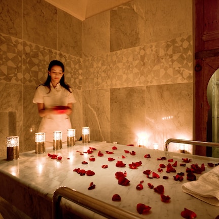 A marble-tiled room with a bed, candles, and rose petals.