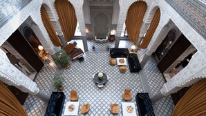 Une cour richement décorée, avec une fontaine centrale, des espaces aménagés pour s’asseoir et des motifs complexes réalisés en mosaïque.