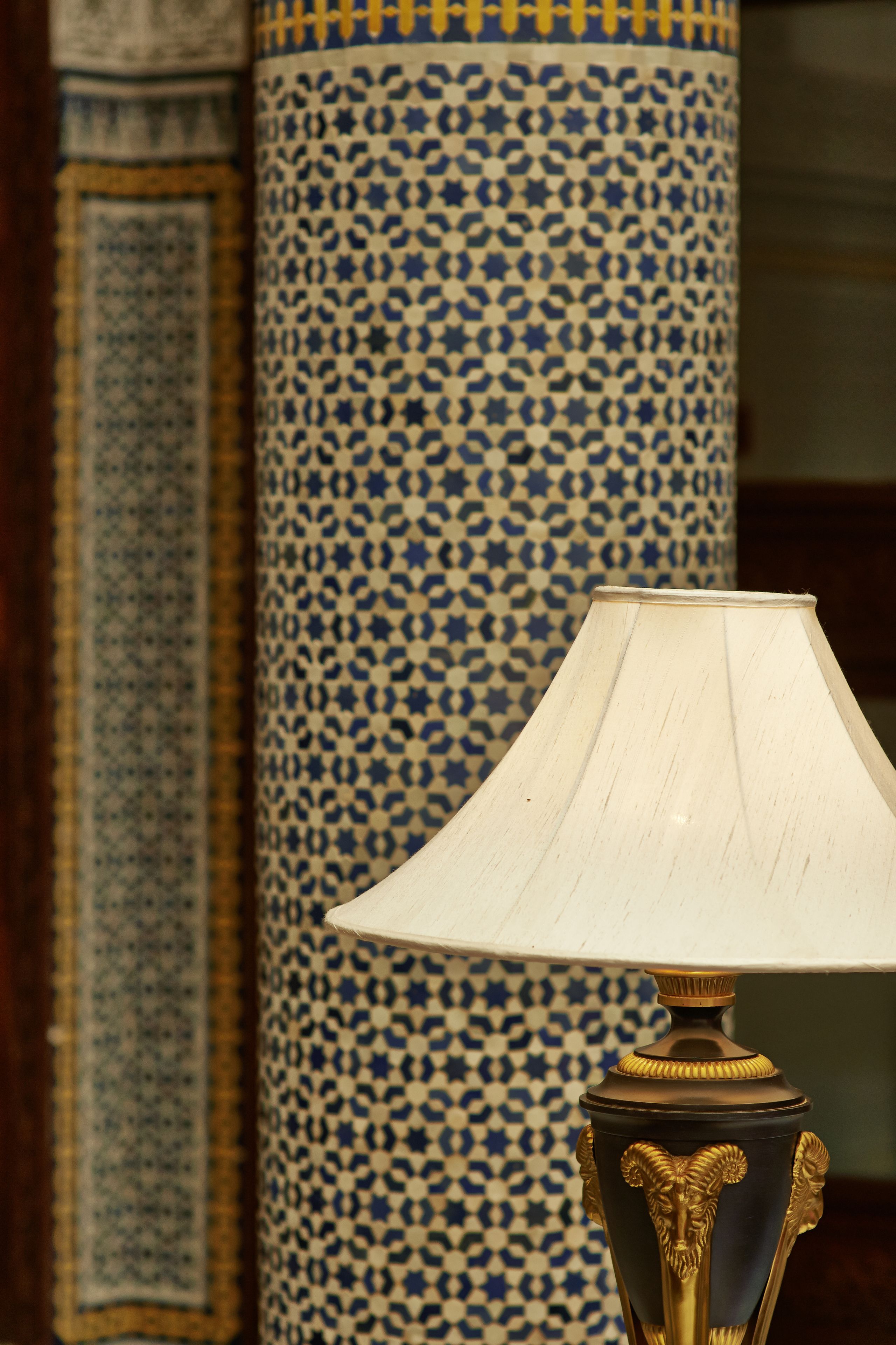 A lamp with a white shade and a decorative base, positioned in front of a tall, intricately patterned column.