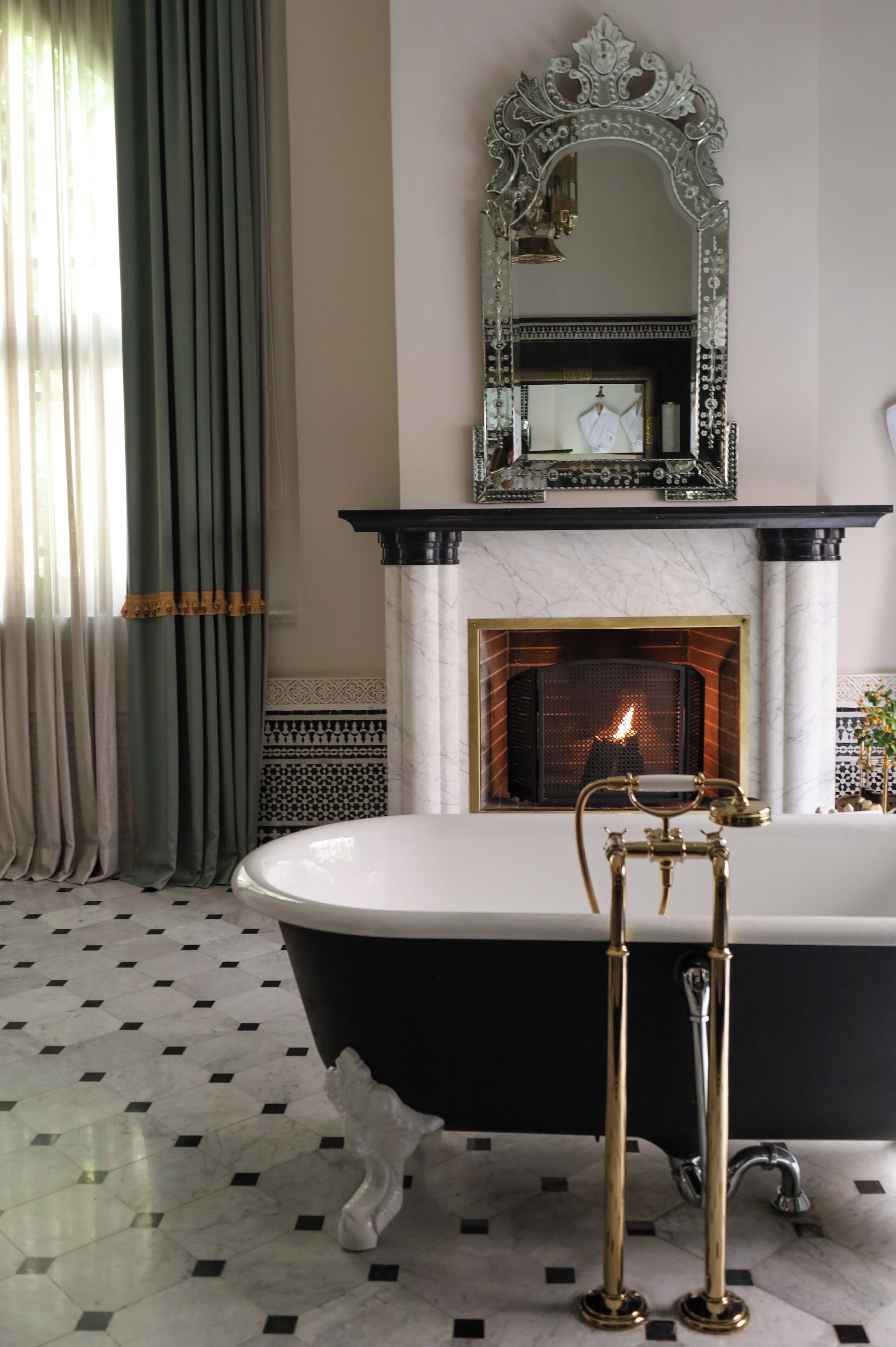 A bathroom with a black bathtub, a white marble fireplace, and a large mirror above the fireplace.